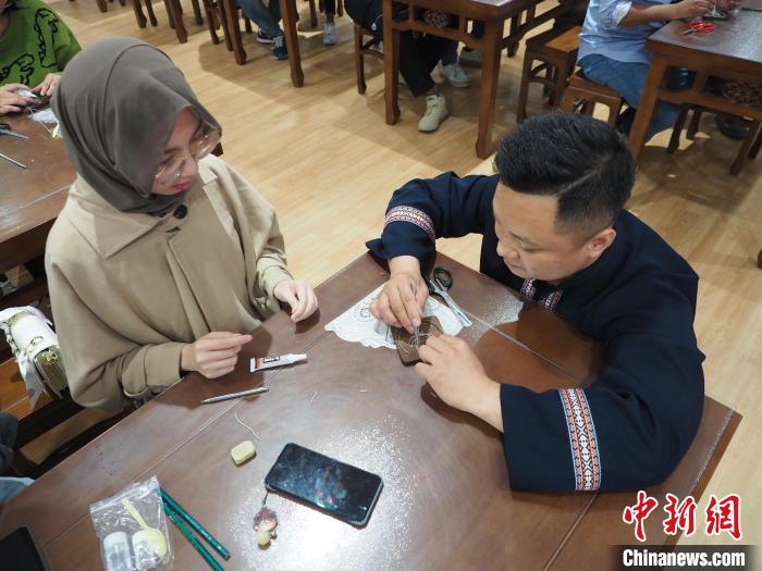 图为工作人员在指导一名留学生制作苗族银饰掐丝画杯垫。 李娇阳 摄 图为工作人员在指导一名留学生制作苗族银饰掐丝画杯垫。 李娇阳 摄