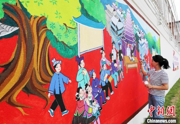 图为侗族农民画家正在外墙上绘制农民画。　龚普康 摄